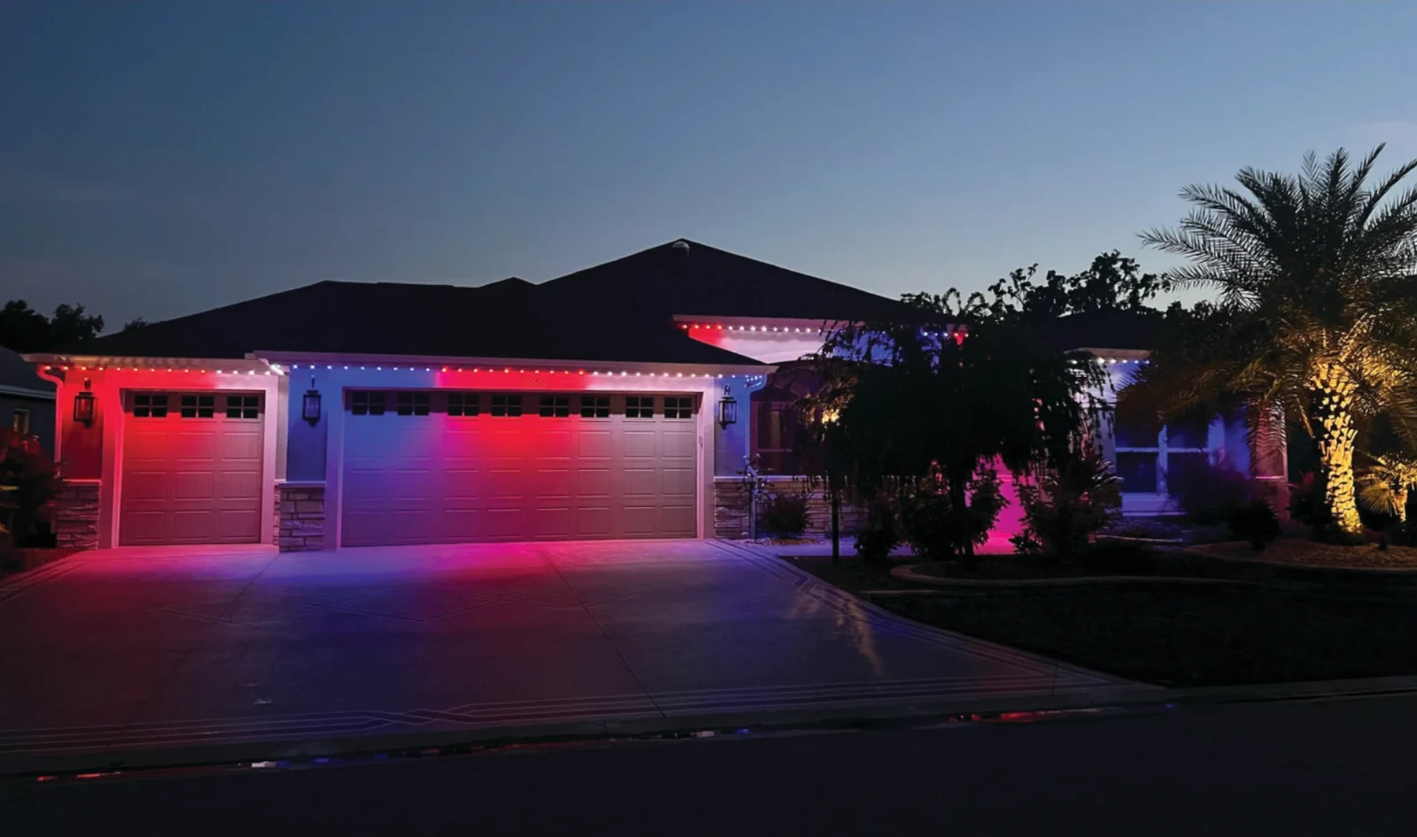 Permanent roofline lighting in red, white, and blue on a home at dusk